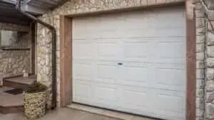 A white sectional garage door set in a stone wall, with a small stone planter by the side entrance.