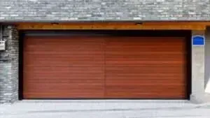 A modern garage door with horizontal reddish-brown wood planks, set into a stone and concrete exterior wall.