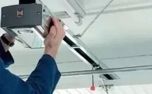 A person in a blue shirt adjusting the motor unit of a ceiling-mounted garage door opener.