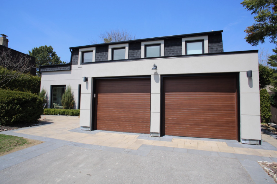 Modern two-story house with double brown garage doors and a paved driveway under a blue sky