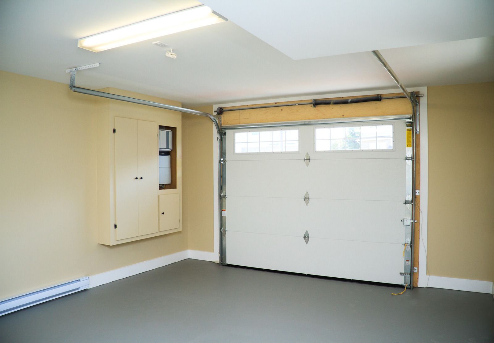 Empty residential garage with white overhead door, beige walls, and a ceiling light