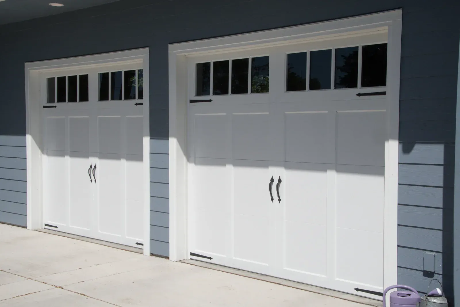 Two white garage doors on a gray house exterior
