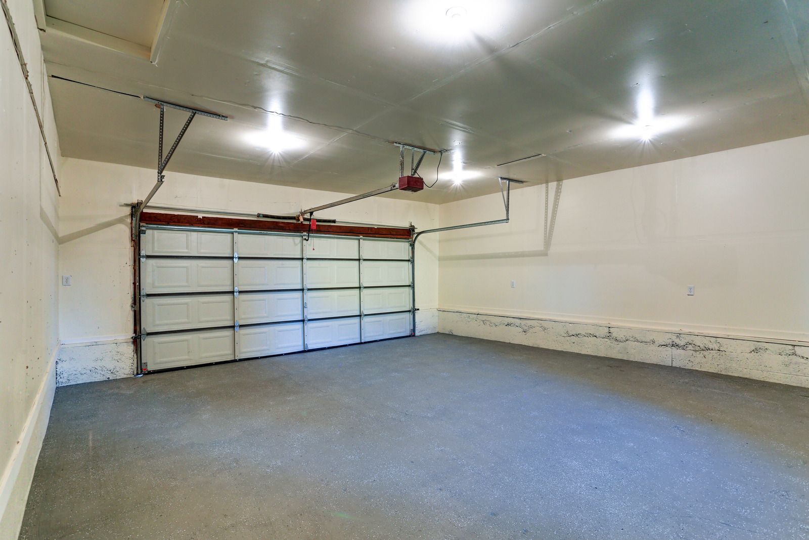 Empty garage with closed white overhead door, gray floor, and ceiling lights