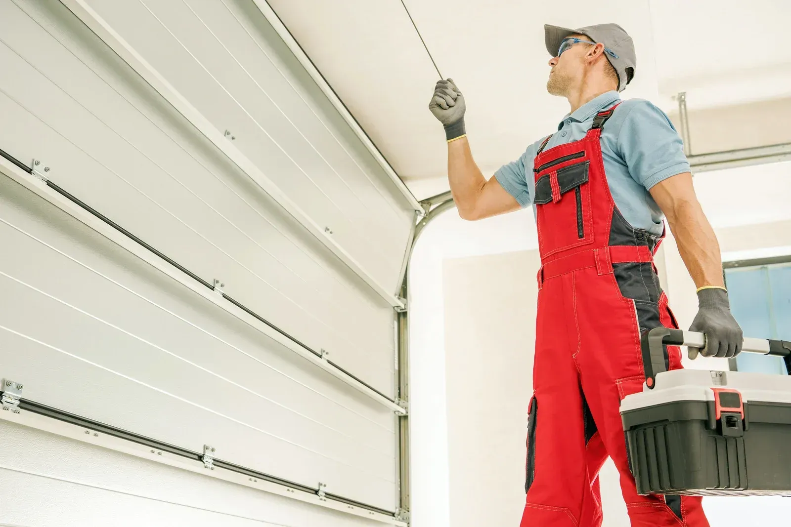Worker in red overalls inspecting a garage door track with a toolbox