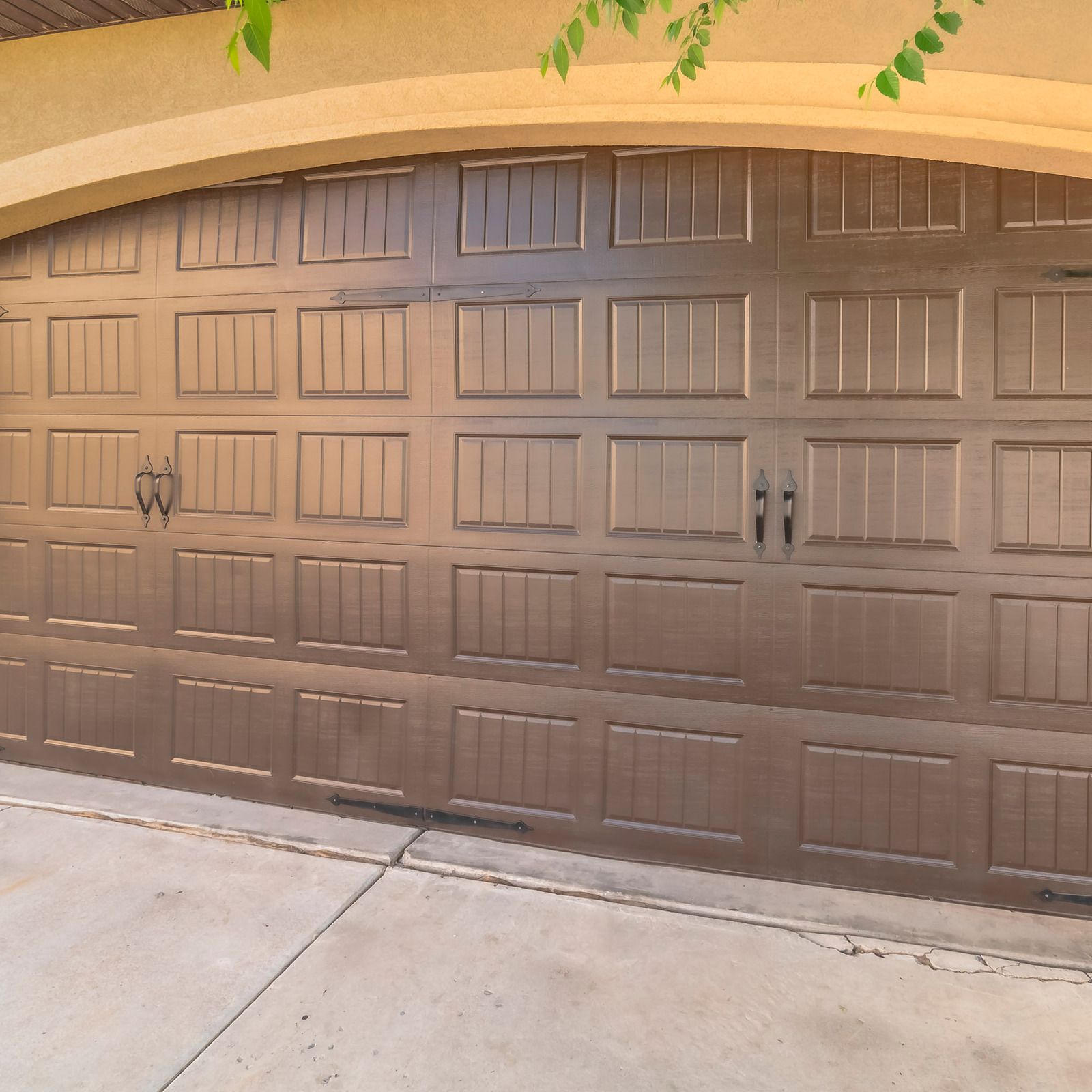 Brown paneled garage door on a beige stucco house, viewed from the driveway.