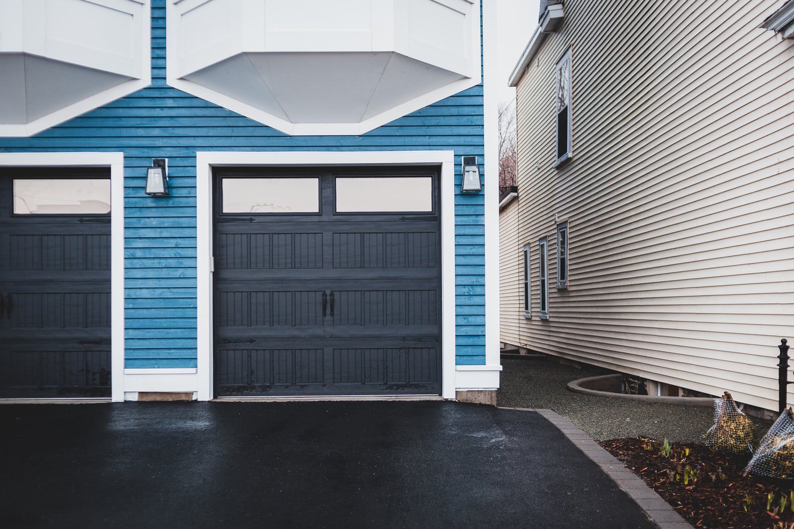 Blue townhouse garages beside a white-sided house on a wet driveway