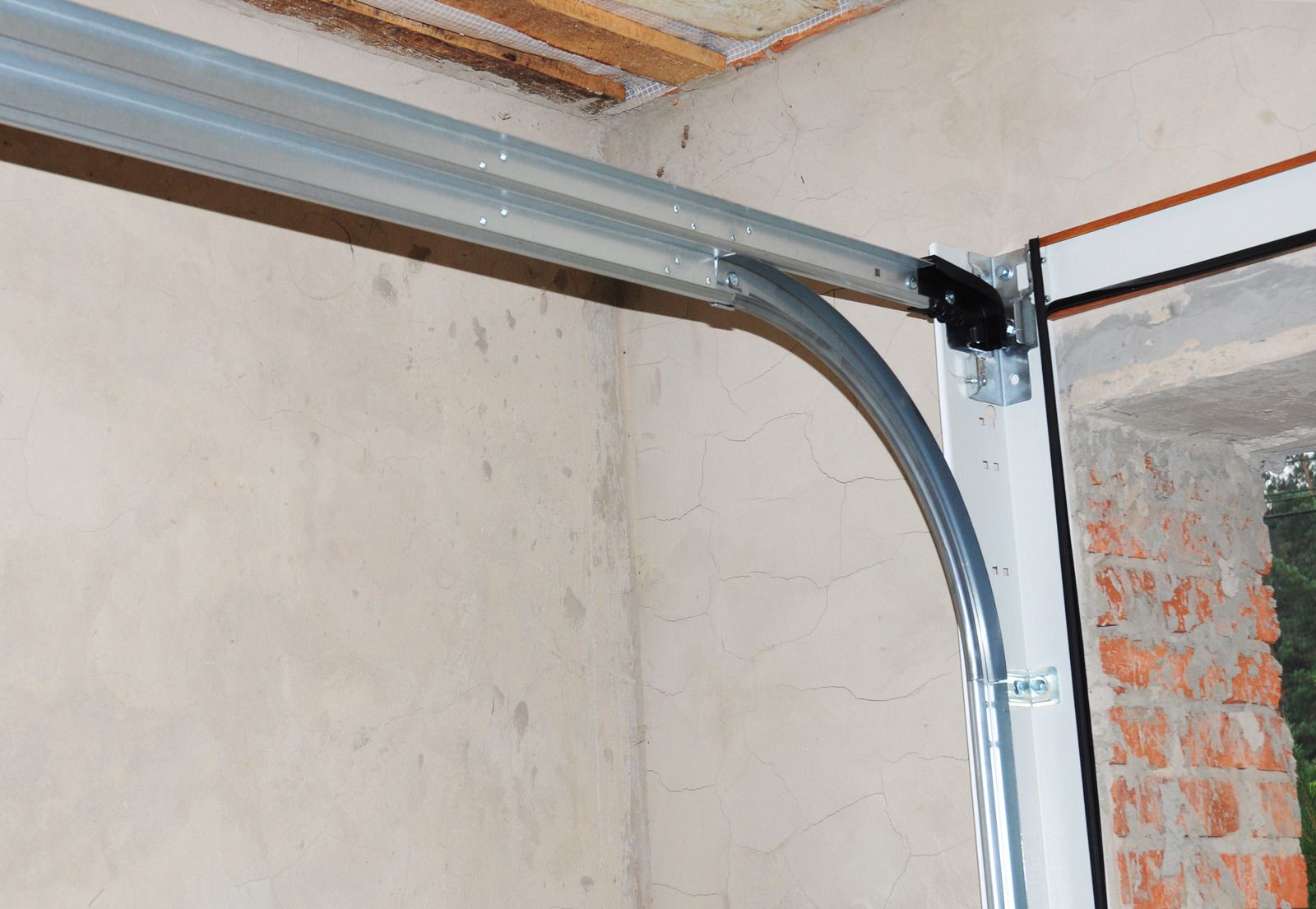 Garage door track and curved metal rail mounted on a wall near a brick opening