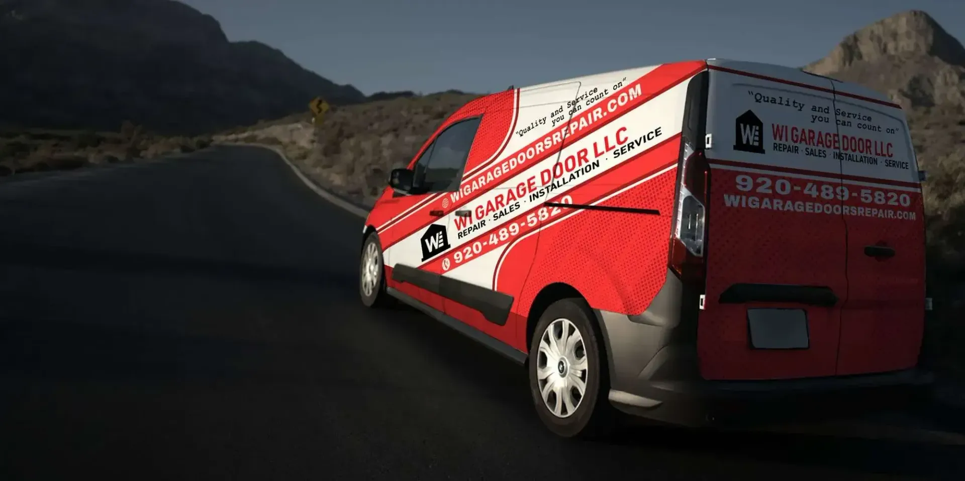 A red and white Garage Door LLC service van driving on a desert road at dusk.