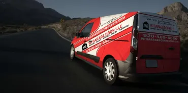 A red and white Garage Door LLC service van driving on a desert road at dusk.