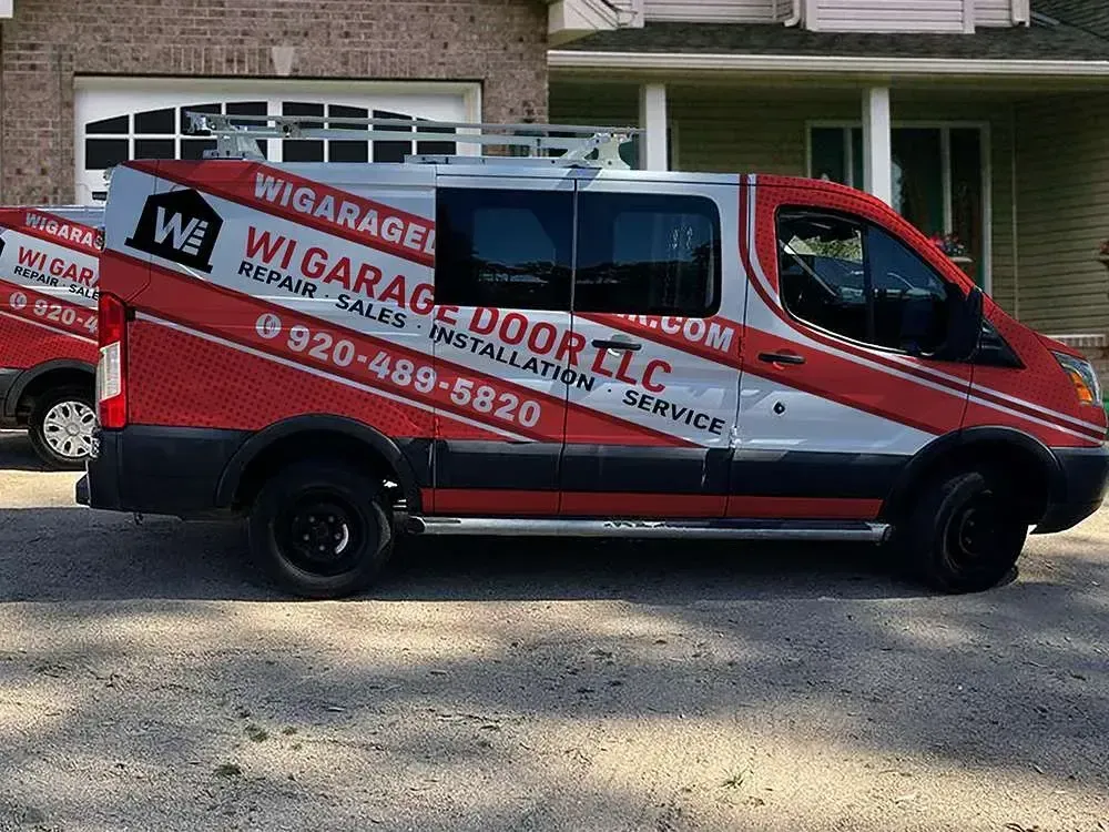 A red and white WI Garage Door LLC service van parked in a driveway in front of a house.