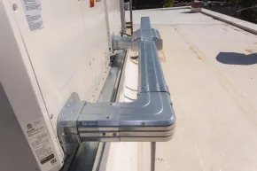 Metal ductwork attached to the side of a white HVAC unit on a flat rooftop.