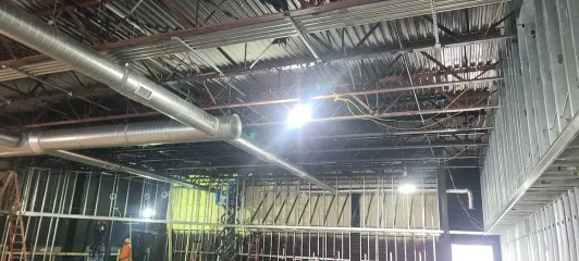 An interior view of a room under construction, featuring exposed industrial ceiling, metal ductwork, and metal wall framing.