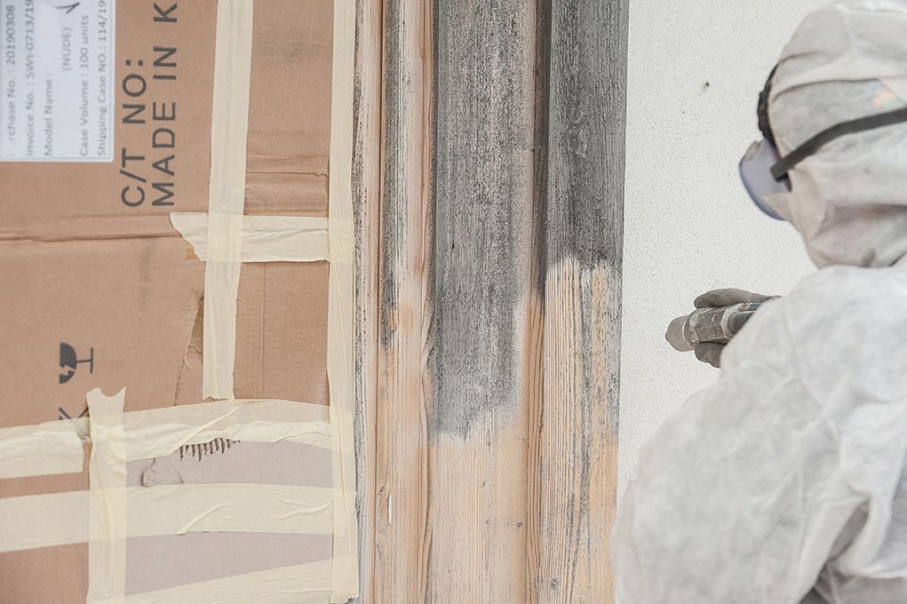 A person in a protective suit is painting a piece of wood