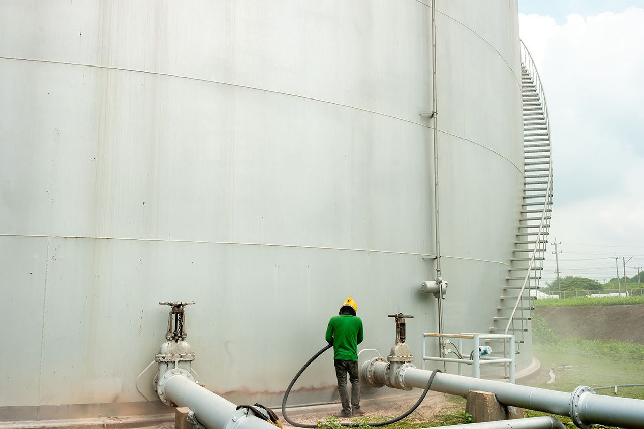 A man in a green jacket is standing next to a large tank.