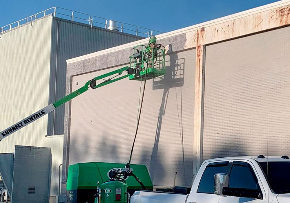 A green crane is cleaning the side of a building next to a white truck.