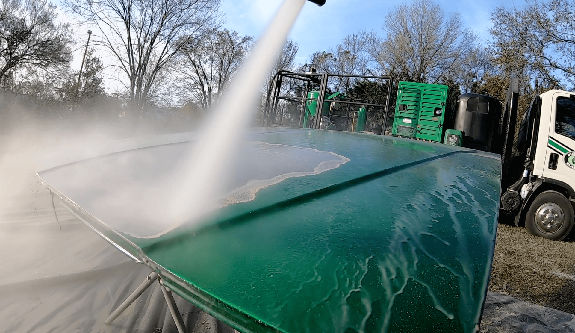 A green trash can is being cleaned with a high pressure washer.