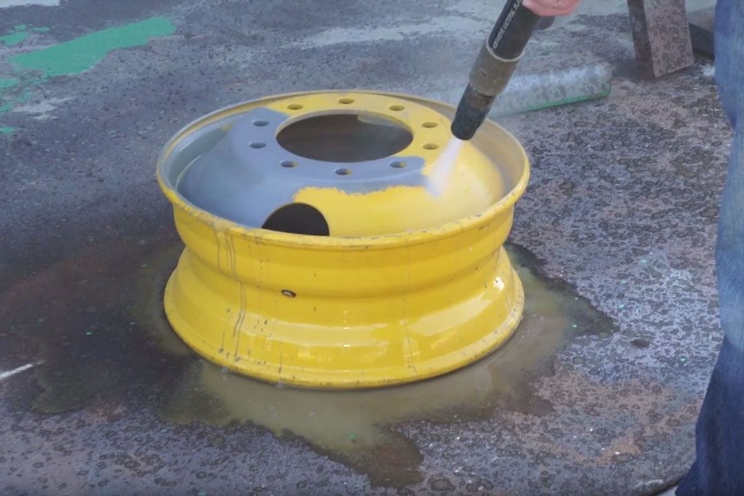 A person is cleaning a yellow wheel with a sprayer.