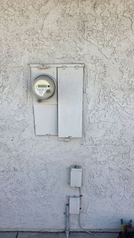 Wall-mounted electric meter and utility boxes on a stucco exterior wall.