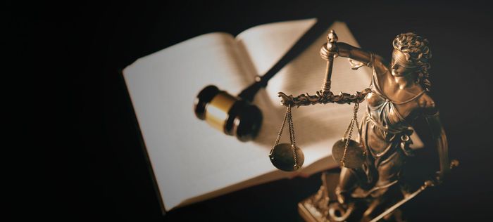 Statue of Lady Justice holding scales, gavel and open book on a dark background.