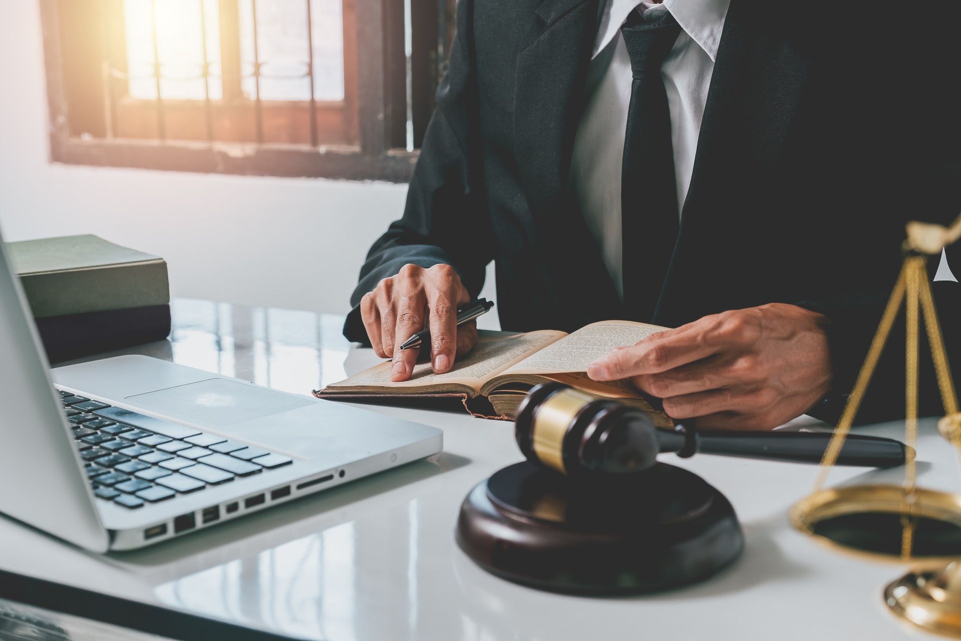 Lawyer in suit reviewing documents, laptop, gavel, and scales on a desk.