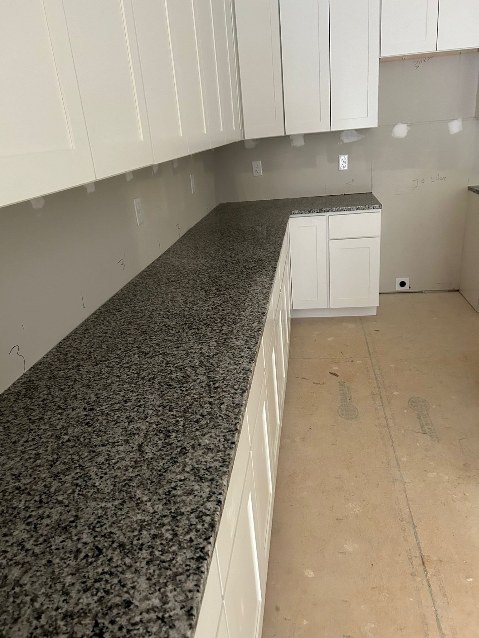 Kitchen under construction, white cabinets and speckled gray countertop.