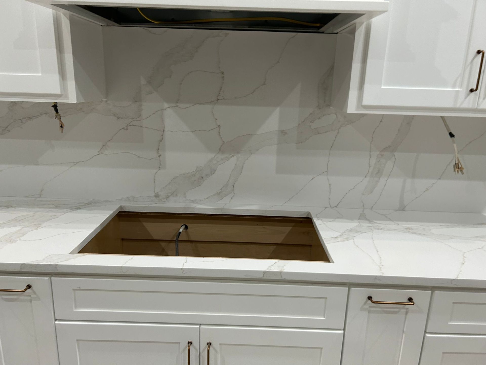 White kitchen with quartz countertop, stove cutout, white cabinets, and marble-like backsplash.