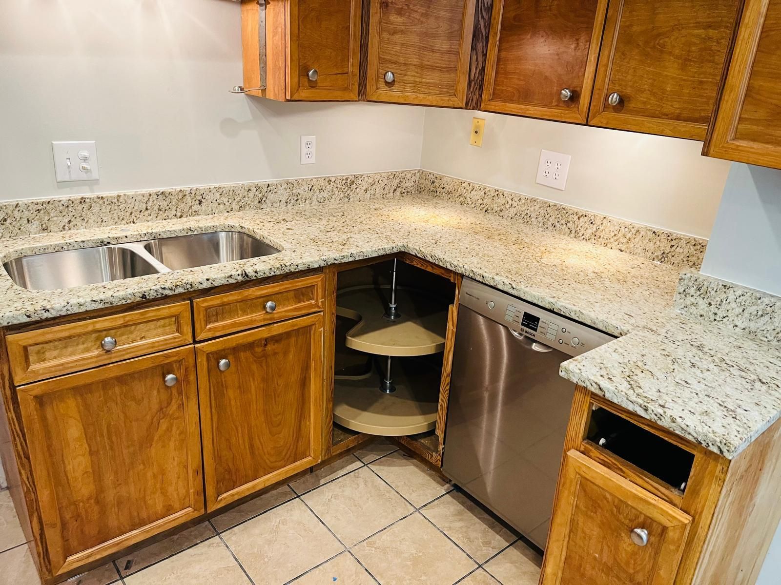 Kitchen with granite countertops, wooden cabinets, a stainless steel dishwasher, and a corner cabinet with shelves.