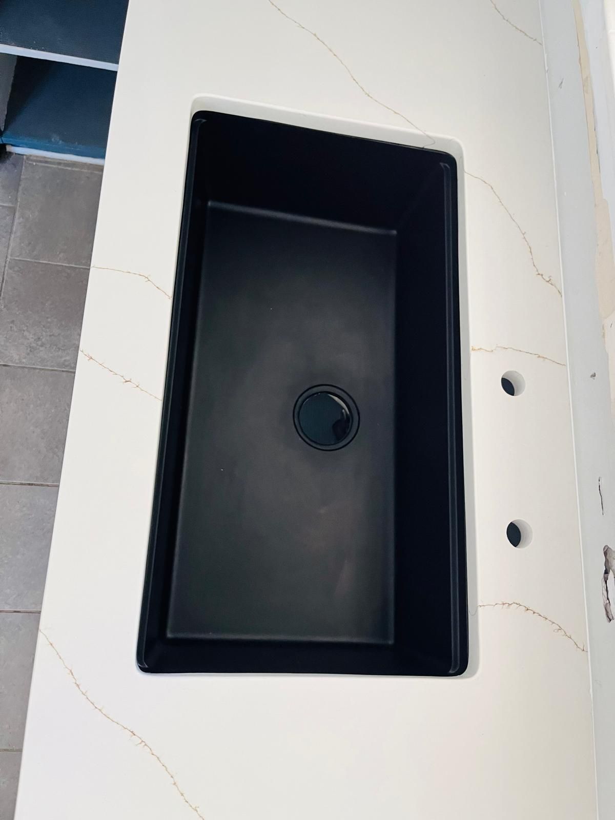 Black rectangular kitchen sink in a white countertop with gold veining.