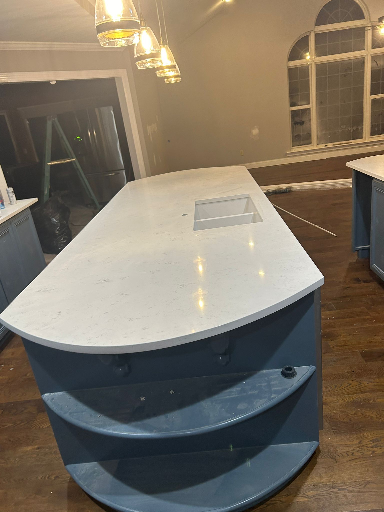Blue kitchen island with white countertop and arched window backdrop.