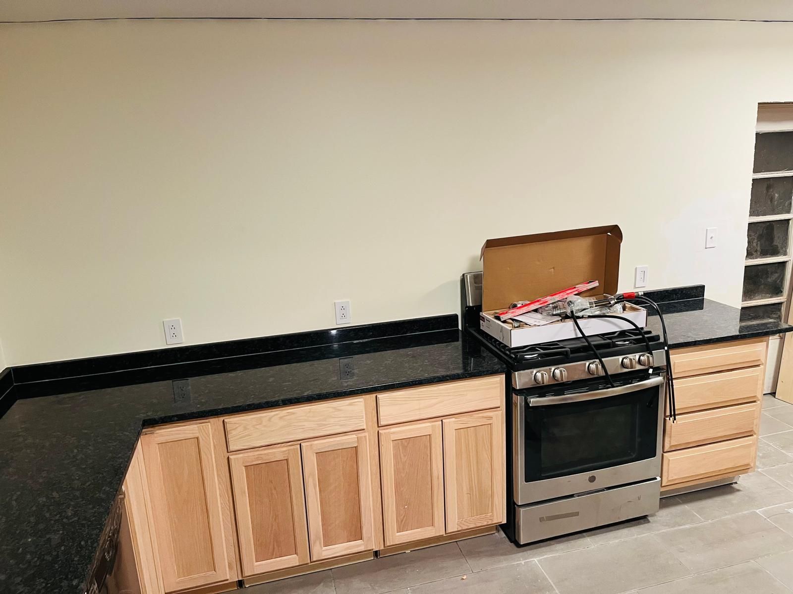 Kitchen under construction with light wood cabinets, black countertop, and stainless steel range.