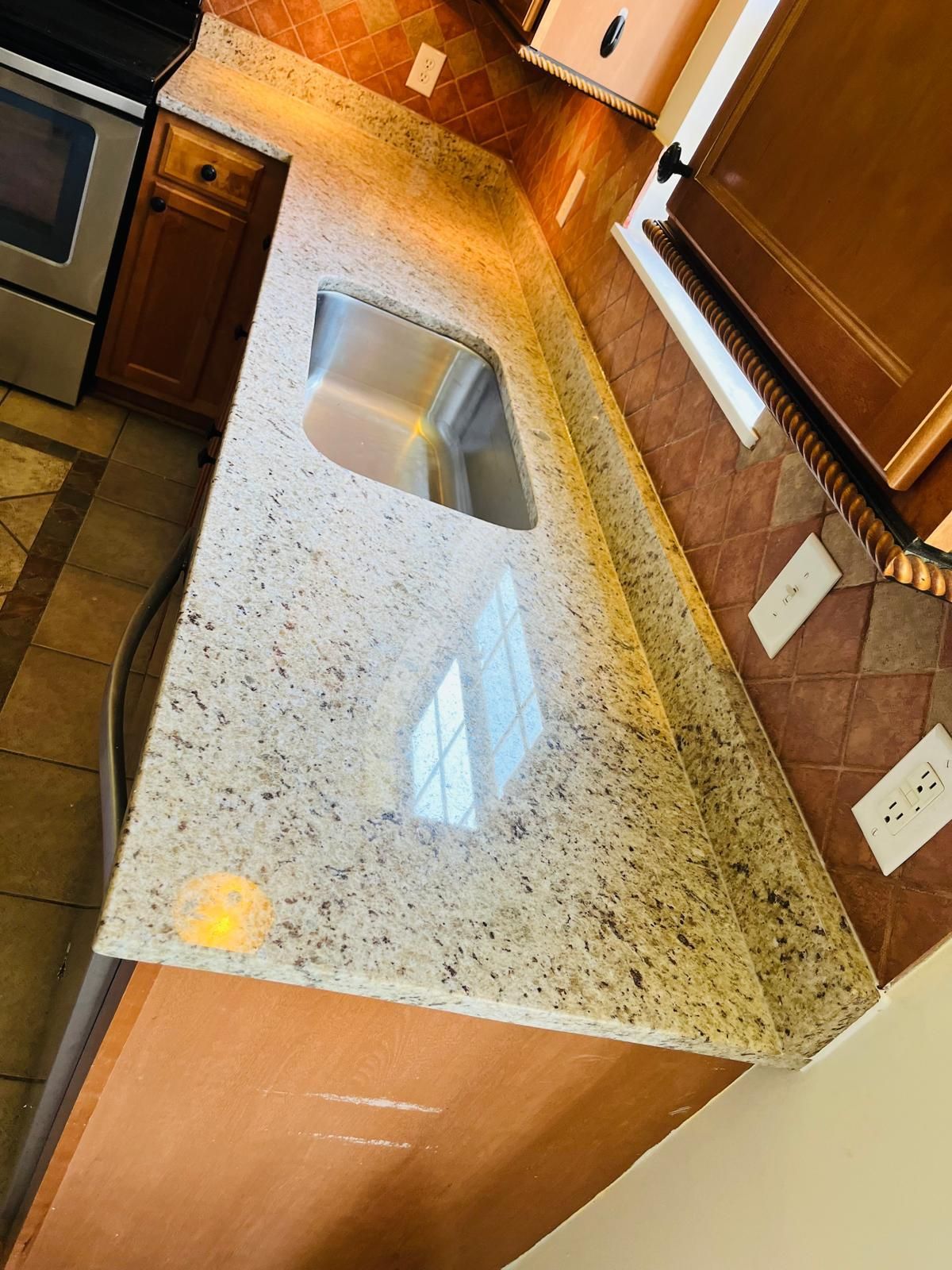 Granite countertop with a stainless steel sink, brown cabinets, and backsplash.