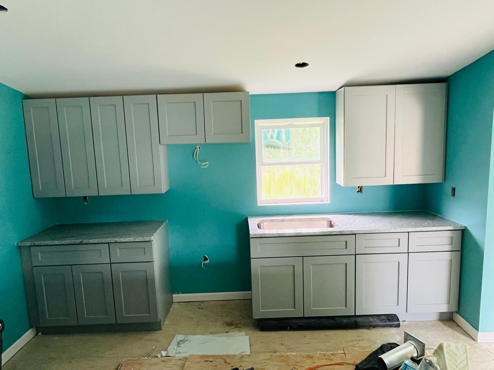 Newly installed kitchen cabinets with countertops against teal walls; the window in the center.