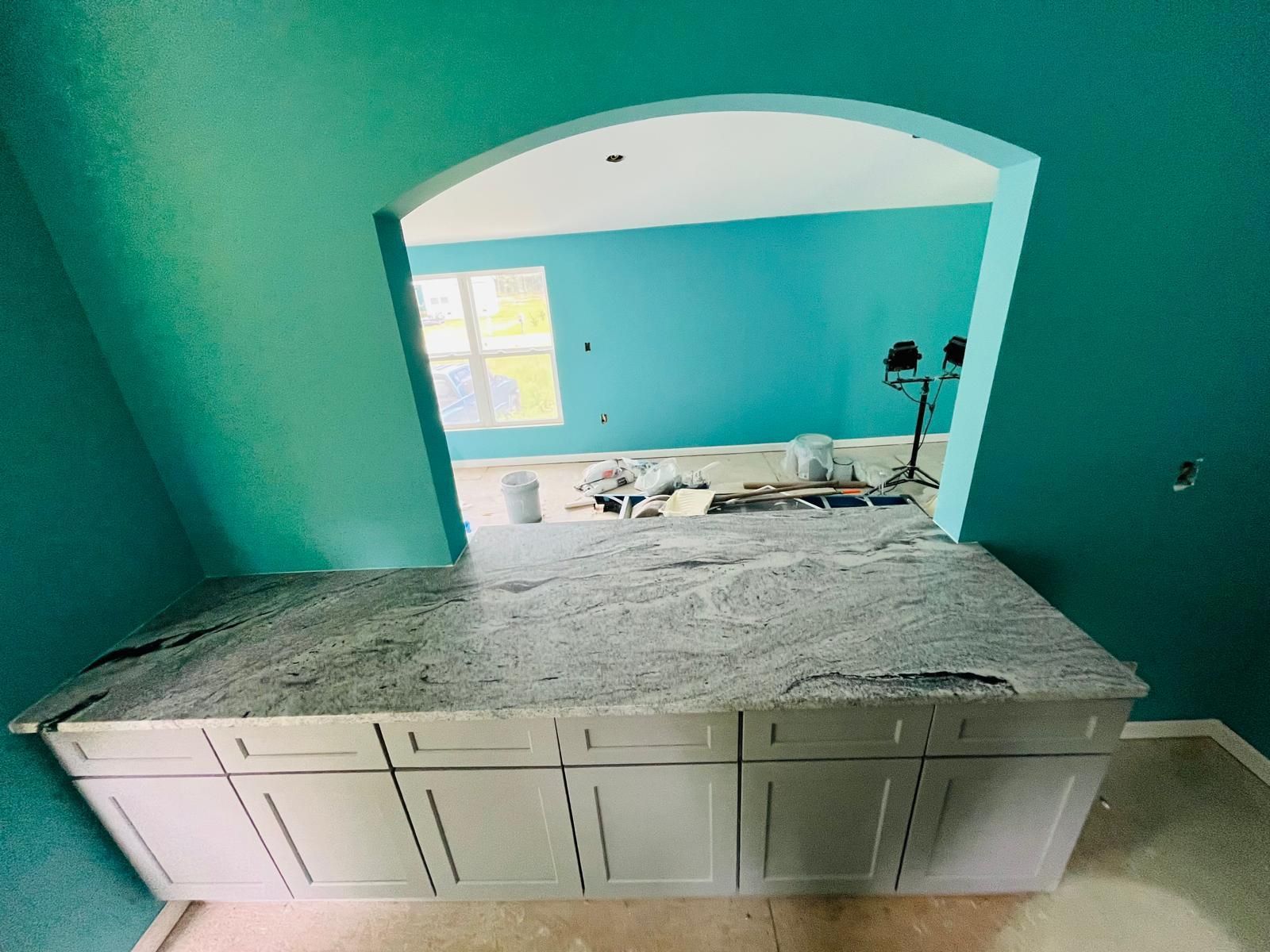 Kitchen area with granite countertop and white cabinets, with a teal archway looking into another room.