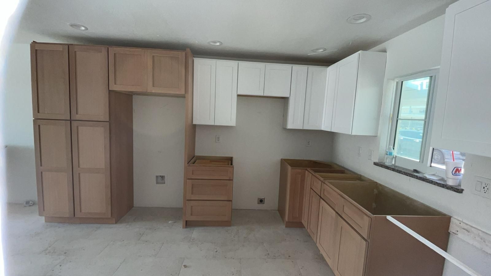 Kitchen cabinets in various stages of installation. Some are white, some light brown. Unfinished construction.