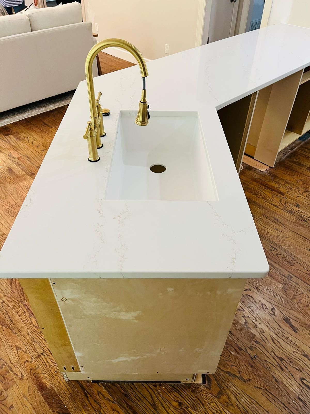 Kitchen island with white countertop, gold faucet, and sink; cabinets unfinished, on wood floor.