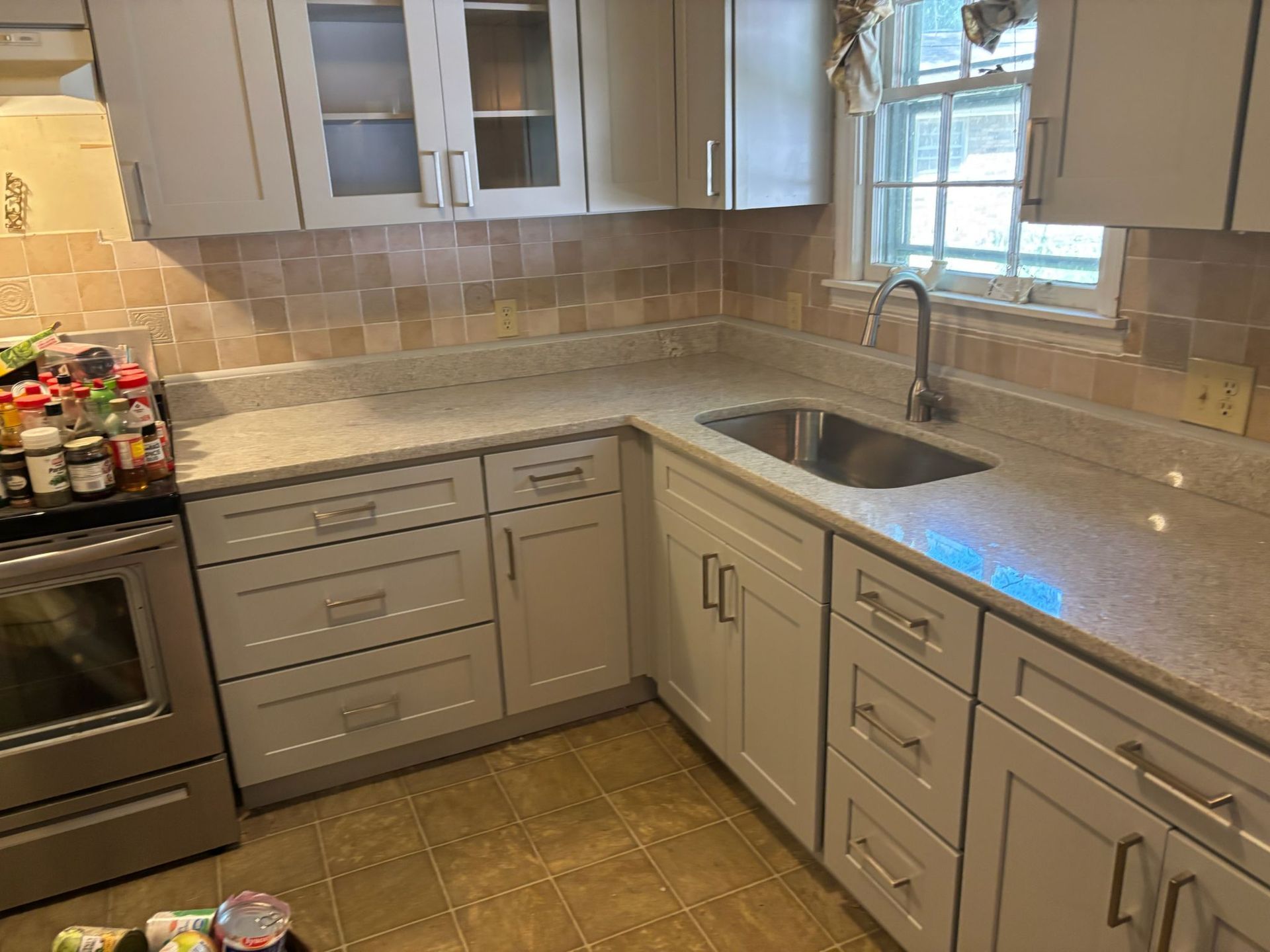 A kitchen with light gray cabinets, granite countertops, and a stainless steel sink.
