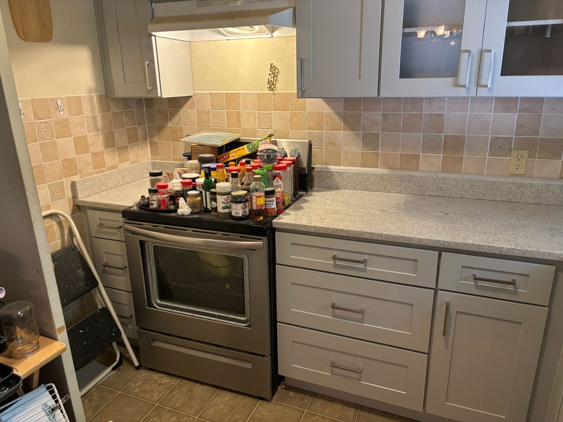 Kitchen with grey cabinets, stainless steel oven, beige backsplash, and spices on the stovetop.