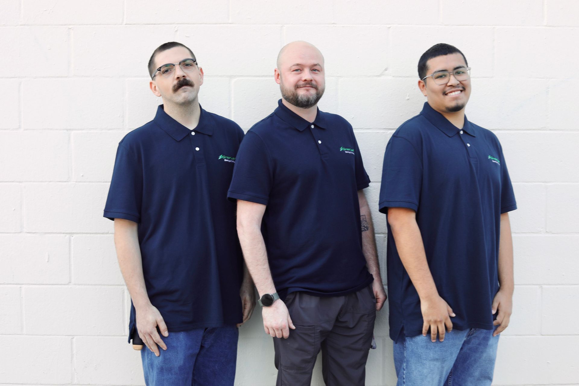 Three men are standing next to each other in front of a tree in a park.