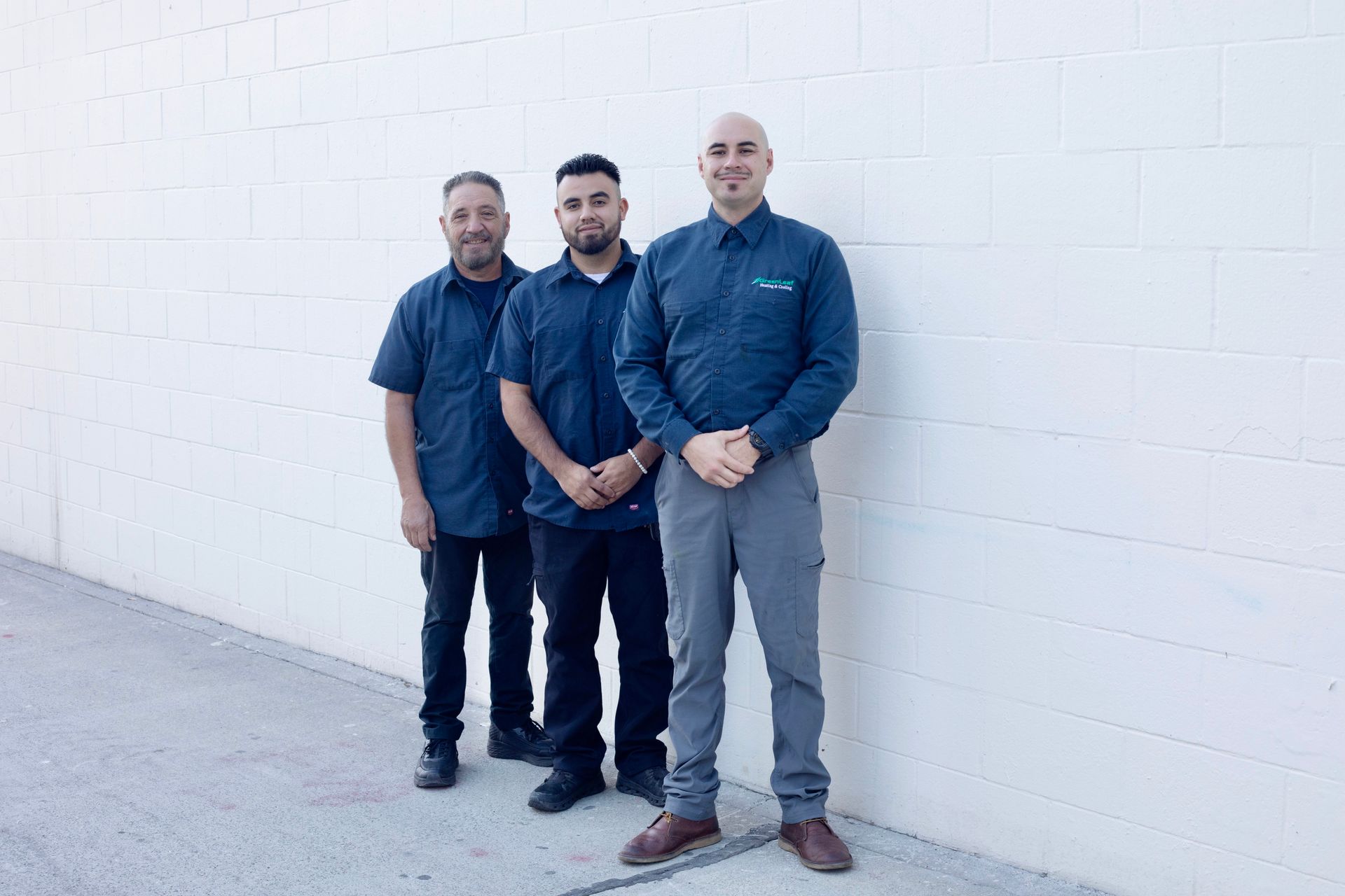 Three men are standing next to each other with their arms crossed in front of a tree.