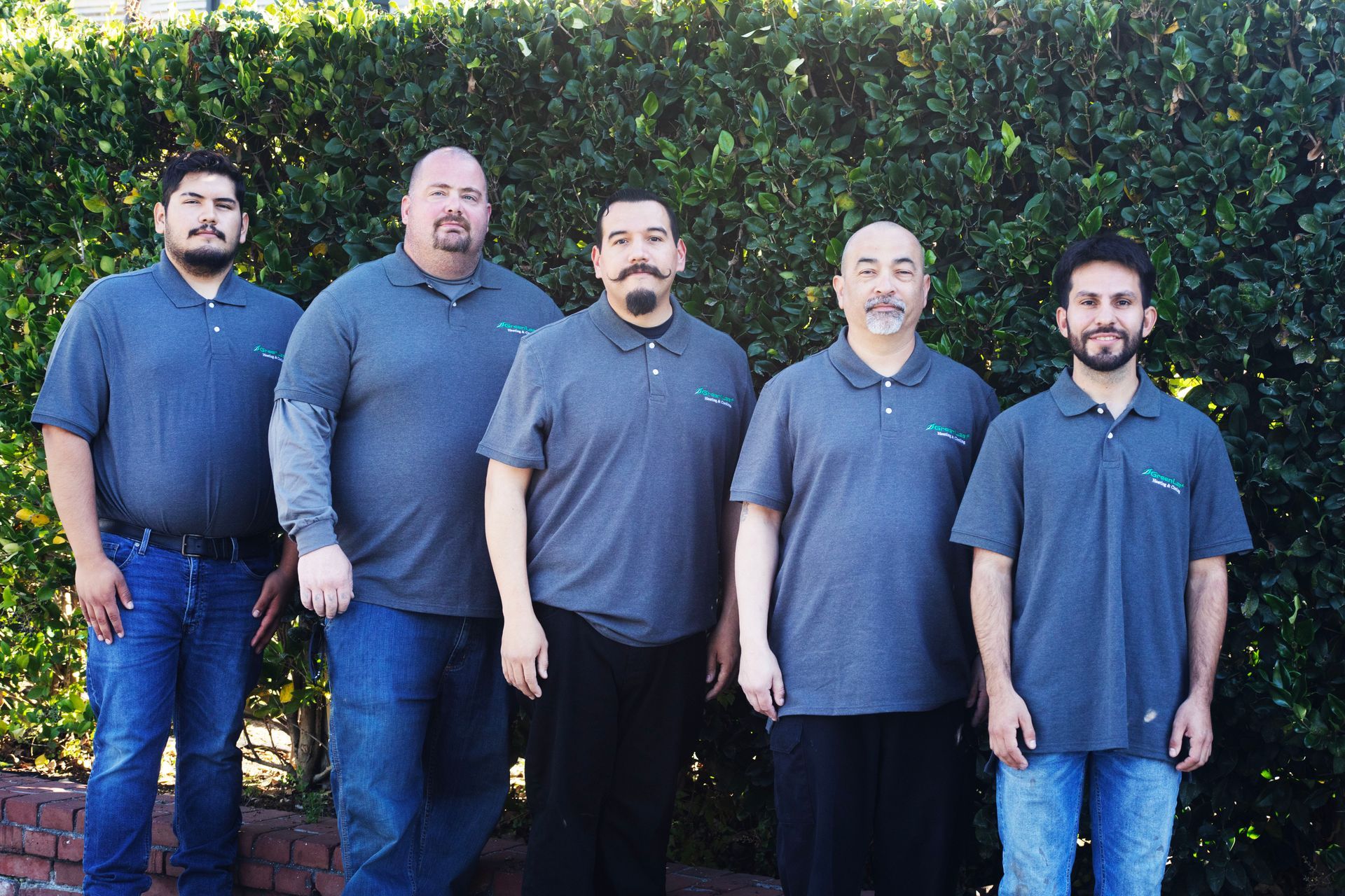 Three men are standing next to each other with their arms crossed in front of a tree.