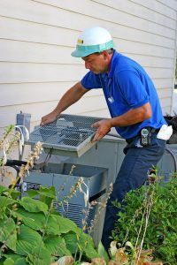 A man wearing a hard hat is working on an air conditioner outside of a house.