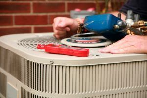 A man is working on an air conditioner outside of a brick building.