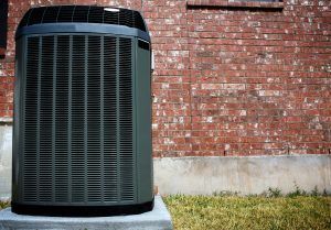 A large air conditioner is sitting in front of a brick building.