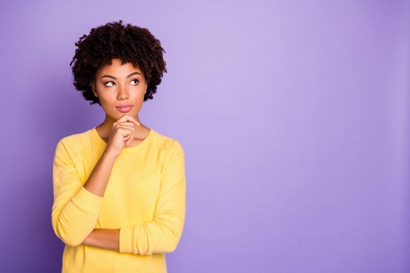 A woman in a yellow sweater is thinking on a purple background.