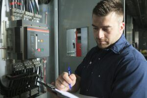 A man is writing on a clipboard in front of an electrical box.