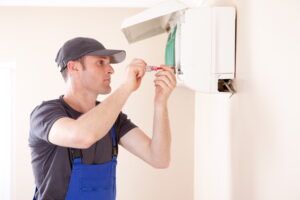 A man is fixing an air conditioner with a screwdriver.