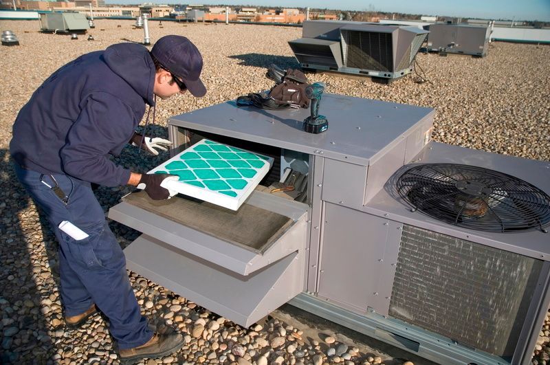 A man is working on an air conditioner on the roof of a building