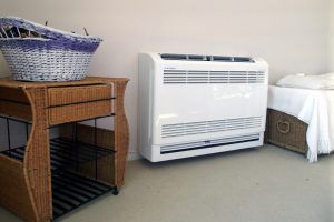 A white air conditioner is sitting next to a wicker table in a room.