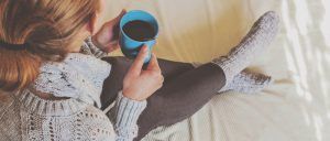 A woman is sitting on a bed holding a cup of coffee.