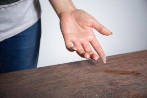 A woman is touching a wooden table with her hand.